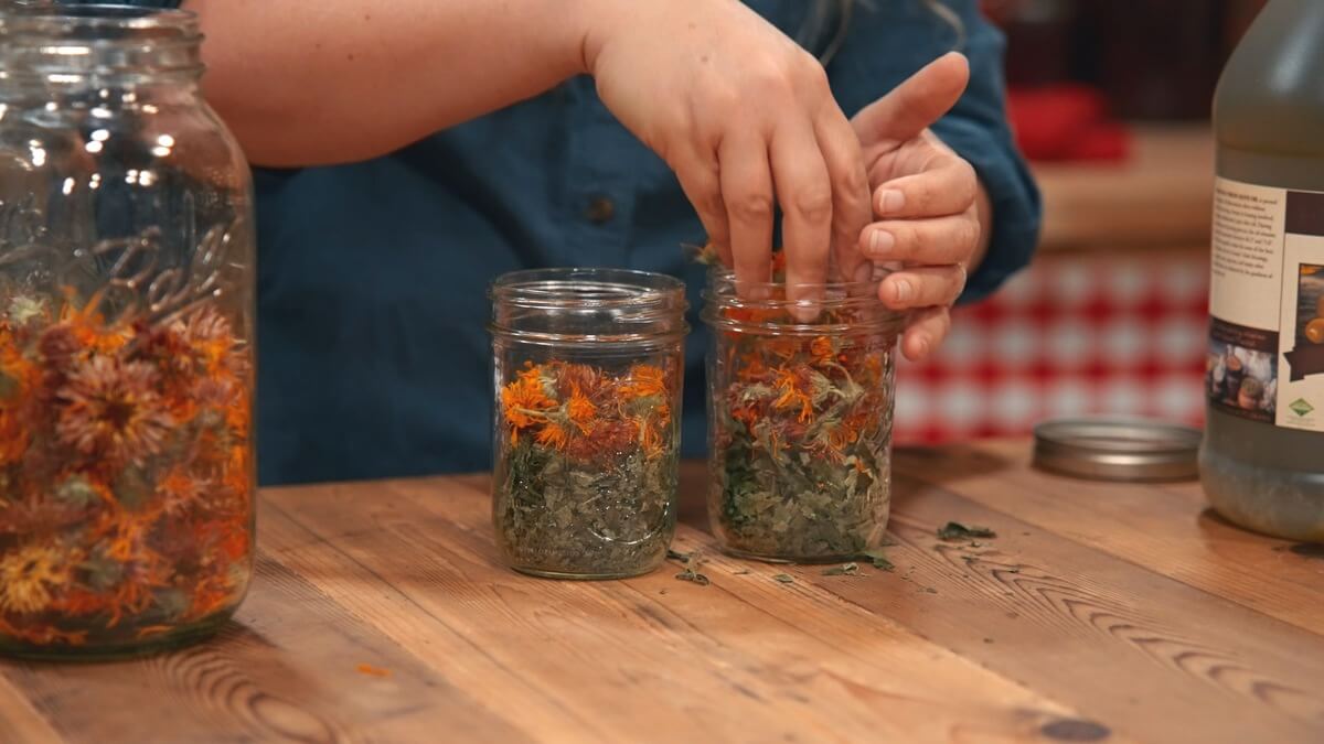 Dried herbs being pushed into a Mason jar.