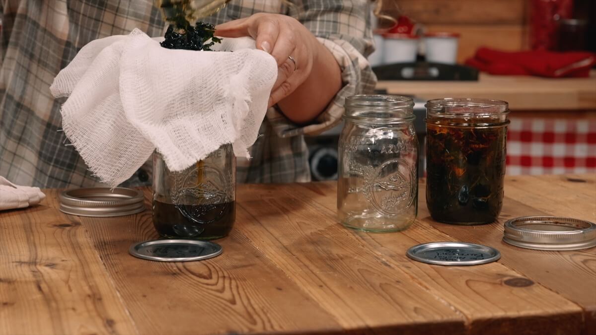 Straining herb infused oil through cheese cloth.