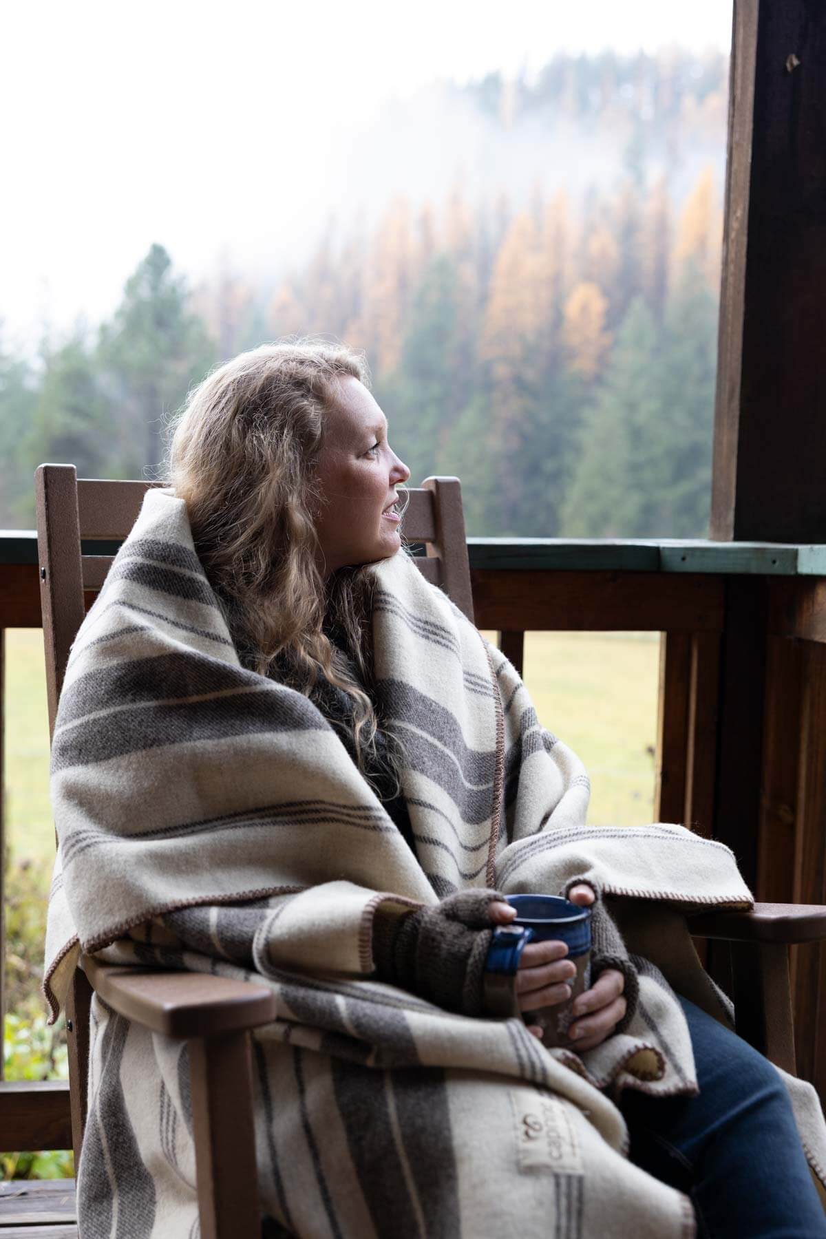 A woman sitting on the porch wrapped in a blanket.
