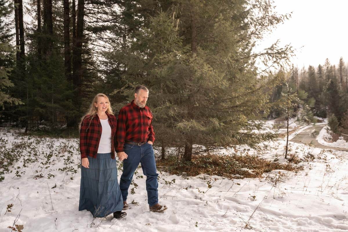 A man and wife walking through the snowy woods.