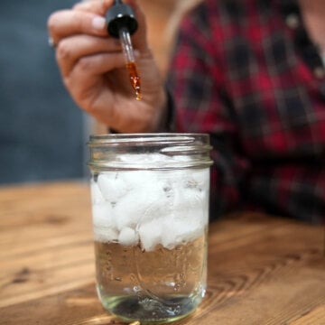 Herbal bitters being added to a jar of sparkling ice water.