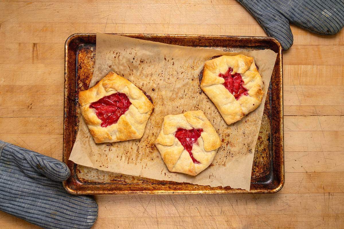 Three golden plum hand held pies on a parchment-lined baking sheet.