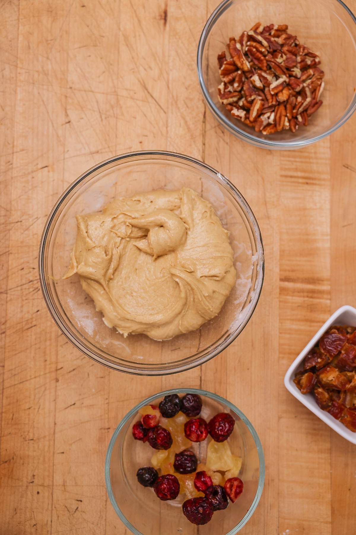 Cookie dough, dried fruit, dates and pecans arranged on a wooden table.
