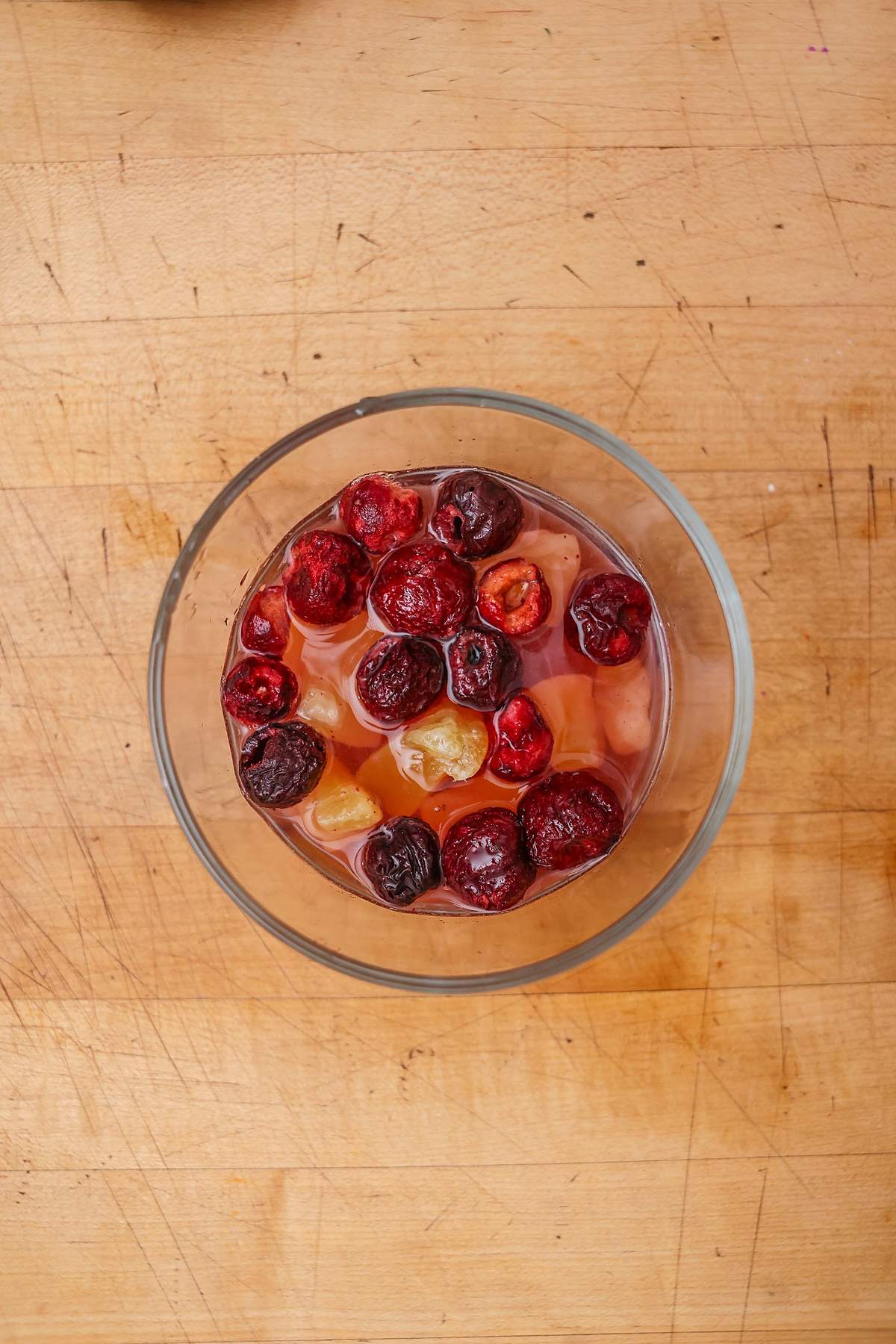 Overhead view of dried fruit in a glass bowl on a wooden table.