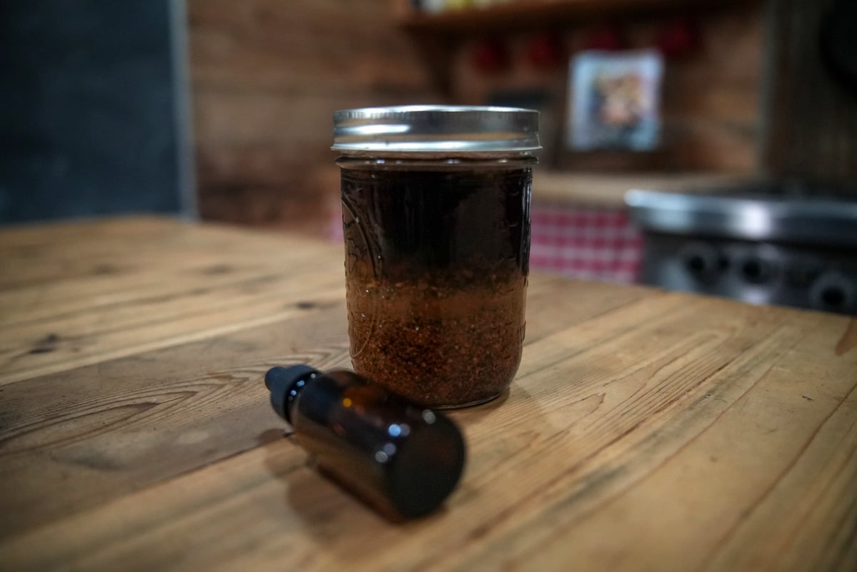 A jar of herbal bitters steeping with a dropper bottle next to it.