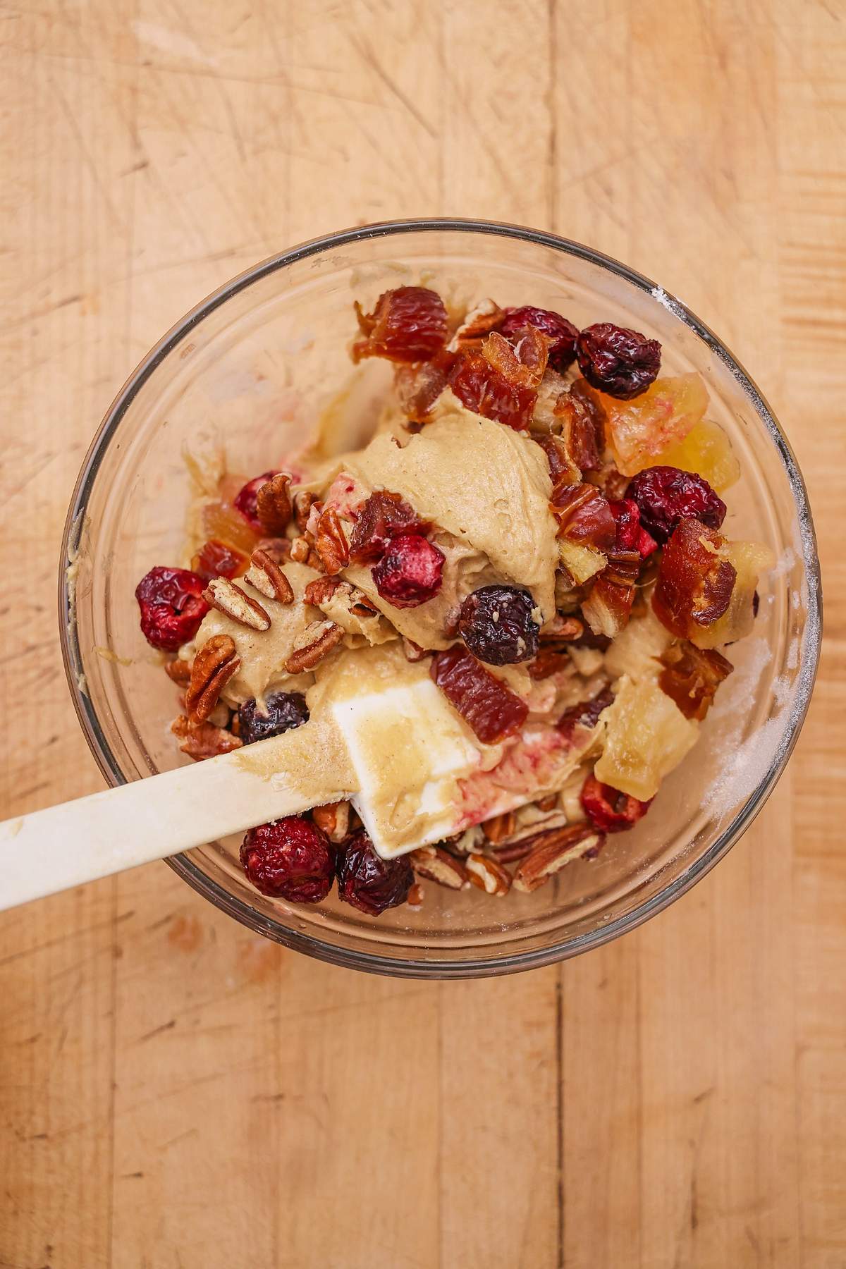 Spatula resting in cookie dough mixed with colorful dried fruit.
