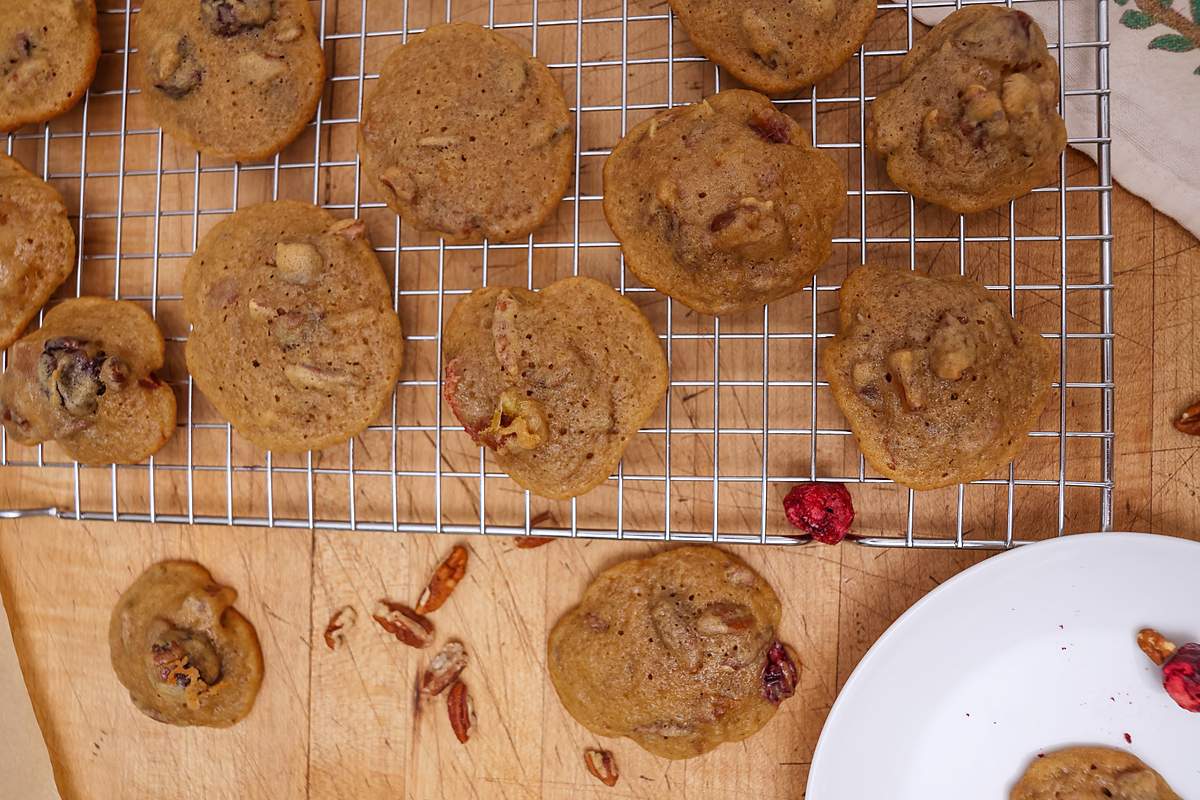 Baked fruitcake cookies on a wire cooling rack with pecans and a white plate nearby.