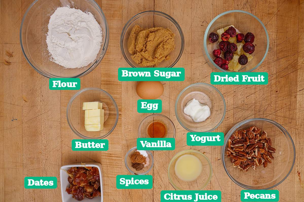 Ingredients for fruitcake cookies arranged in bowls on a wooden table.