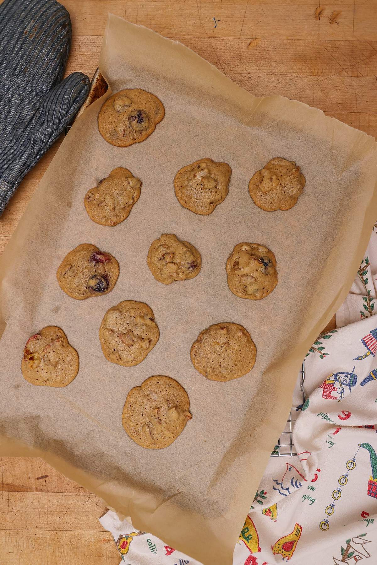 Fruitcake cookies on a parchment-lined baking sheet beside an oven mitt.