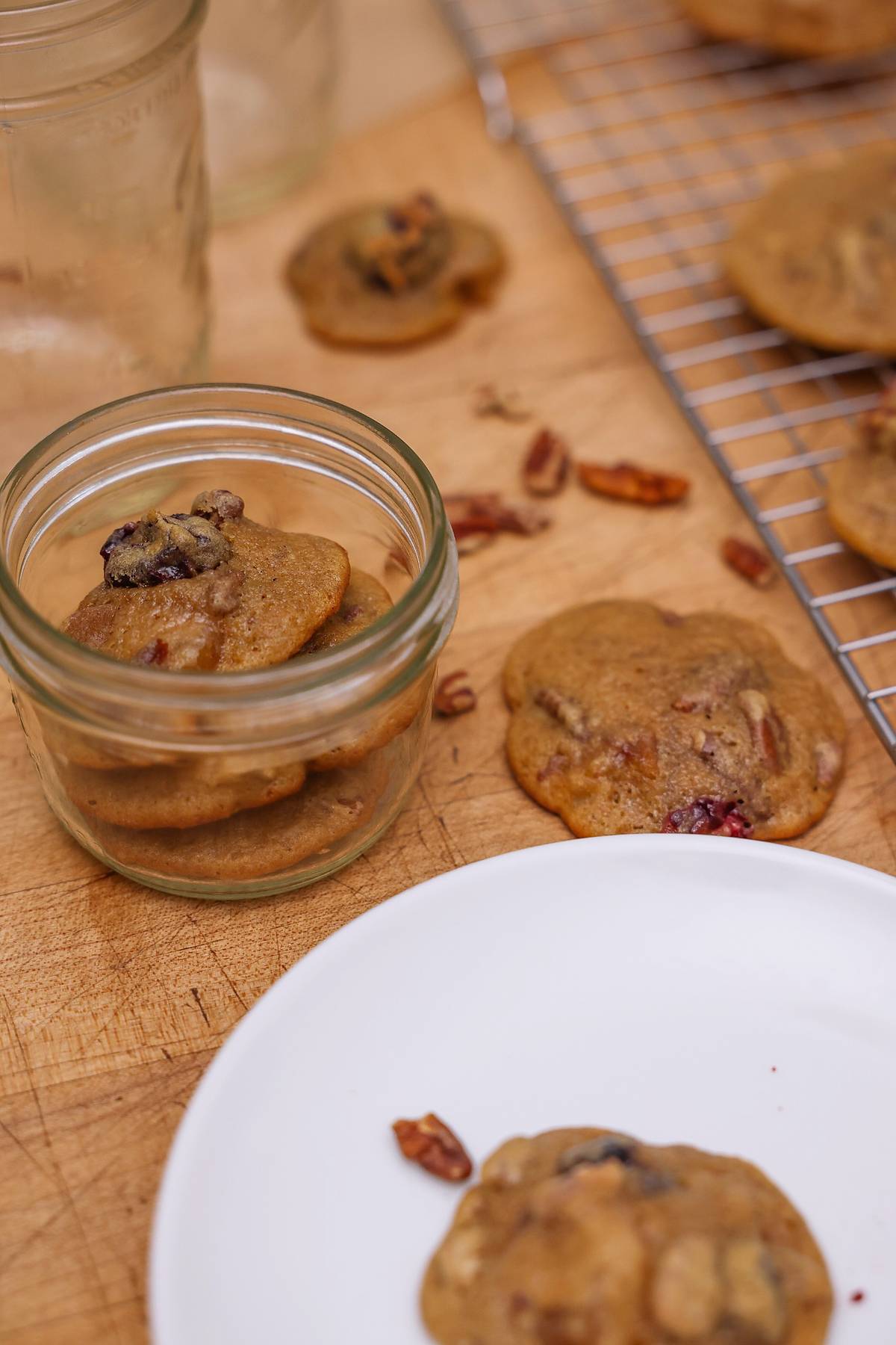 Close-up of a fruitcake cookie on a white plate with more cookies in a glass jar.