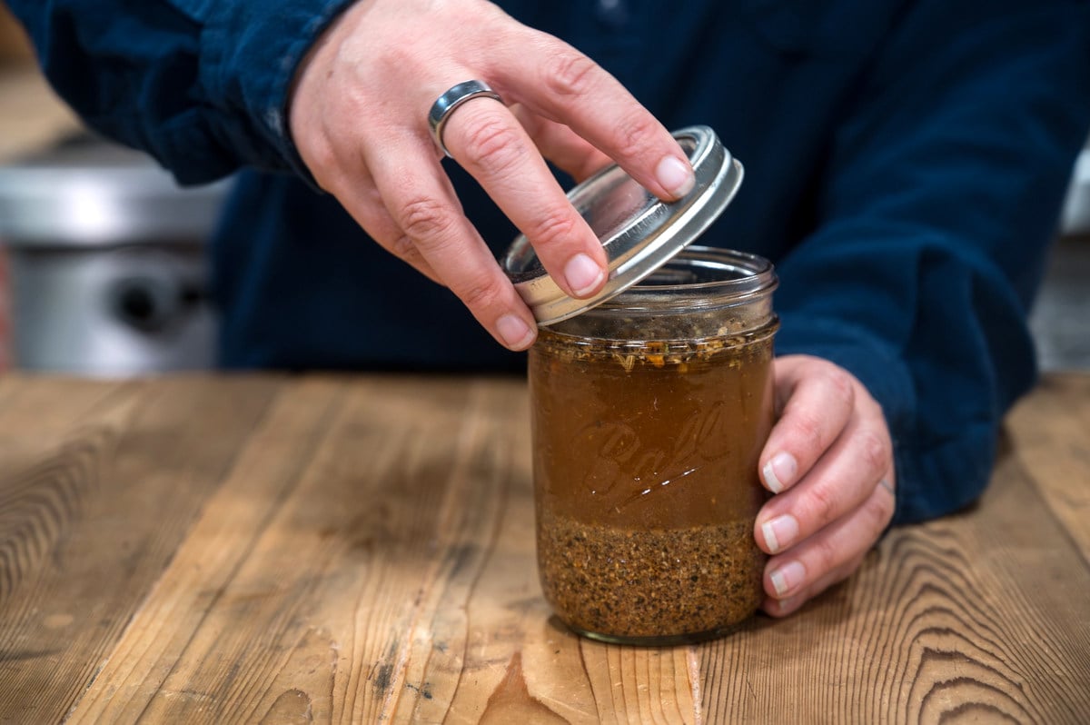 A woman putting a lid onto a jar of herbs steeping in alcohol.