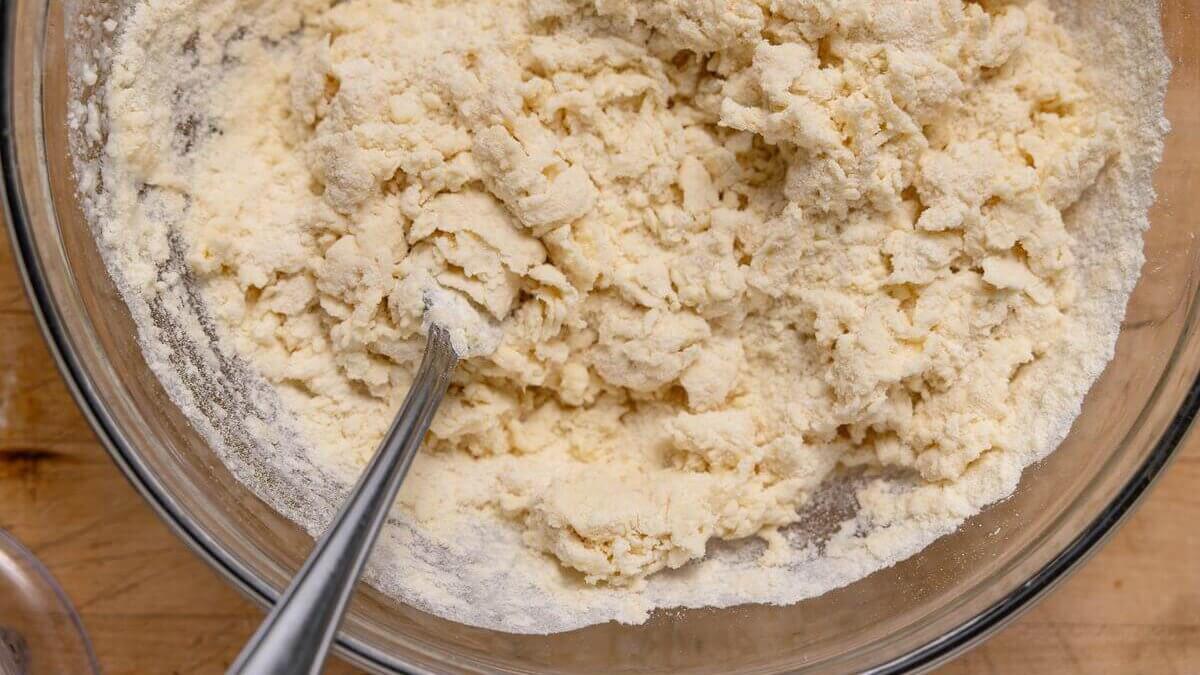 Close-up of a crumbly flour and butter mixture in a glass bowl with a fork for hand held pie pastry.