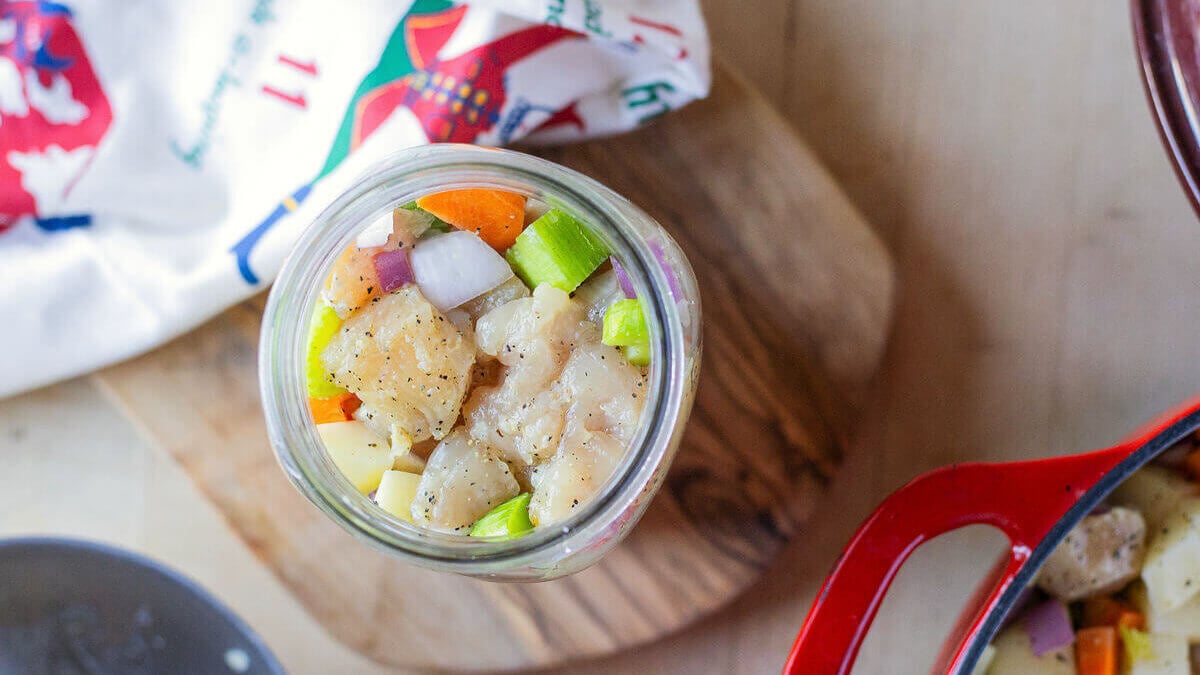 Overhead view of an open jar filled with chicken and chopped vegetables.