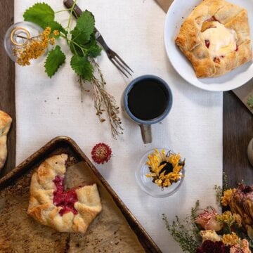 Overhead view of plum pies, coffee mugs, greenery and autumn flowers.