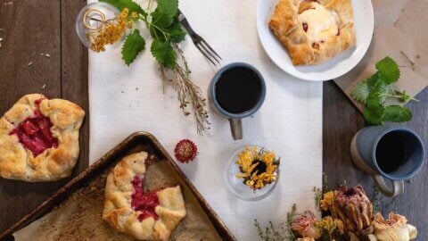 Overhead view of plum pies, coffee mugs, greenery and autumn flowers.