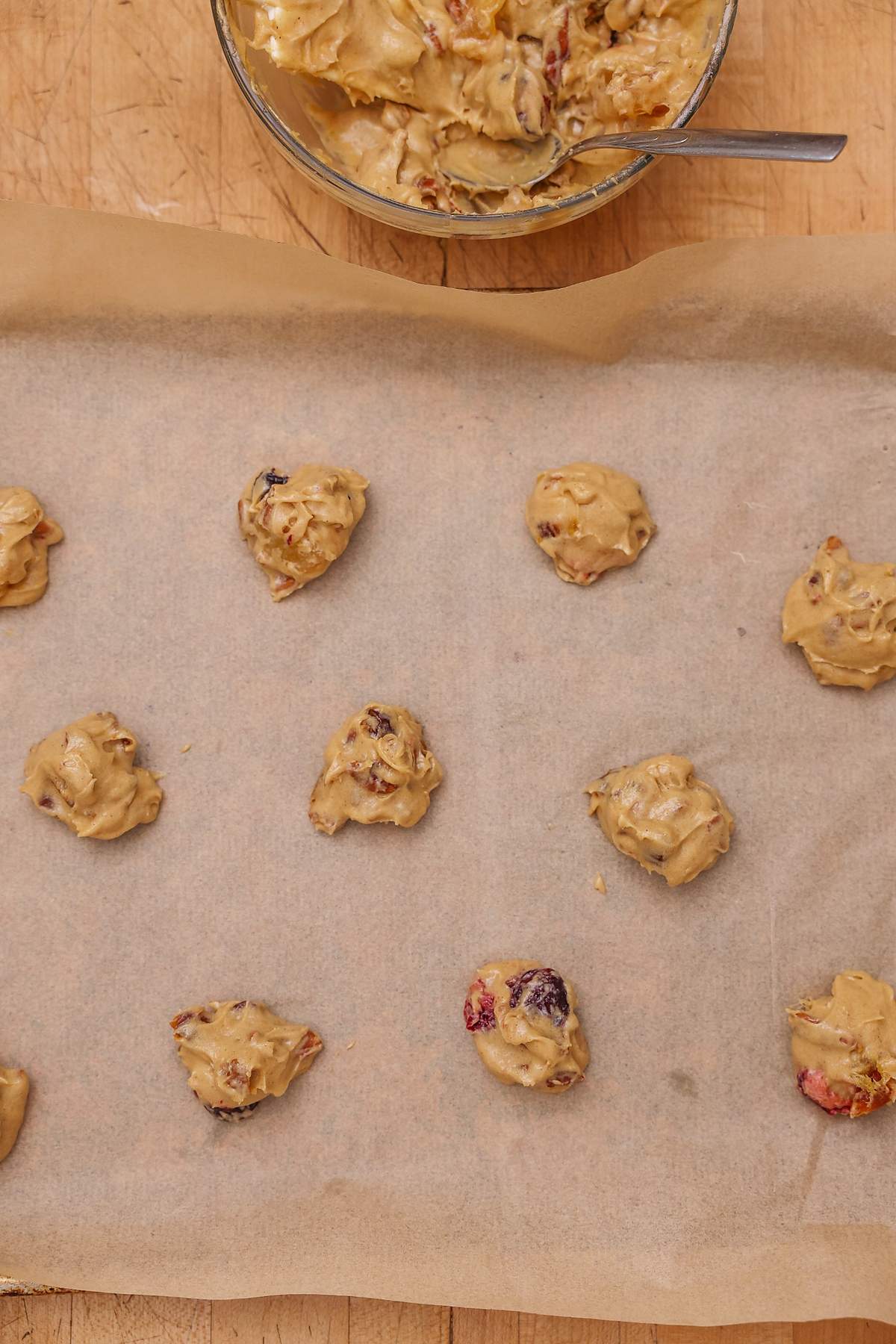 Portions of fruitcake cookie dough on a parchment-lined baking sheet.