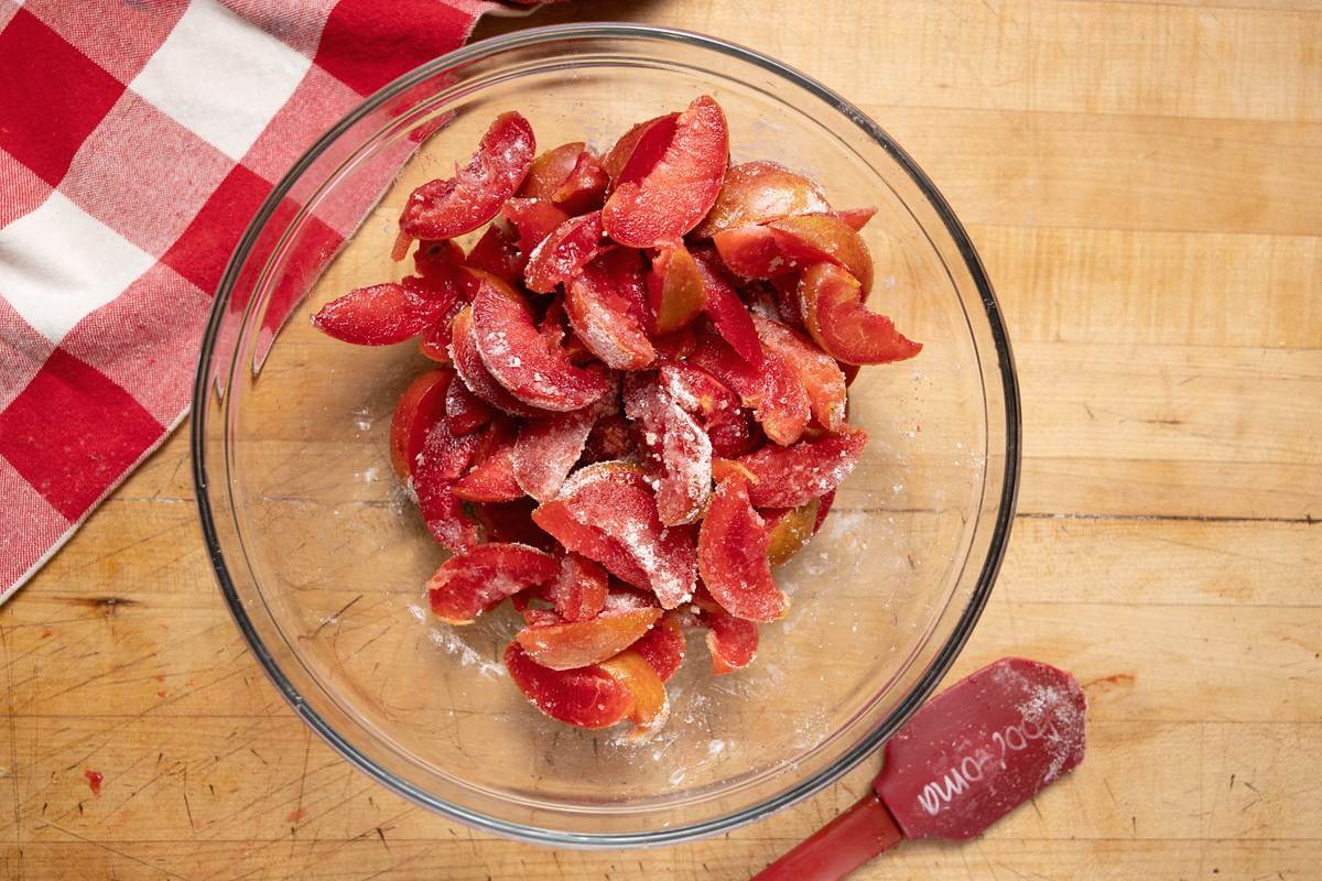 Sliced plums coated with dry filling ingredients in a glass bowl.