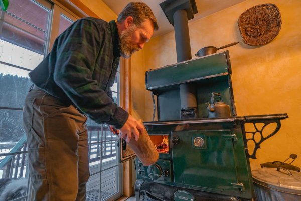 50167528101_76f0fcfe61_k A man adding wood to a wood burning cookstove.