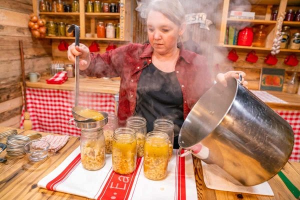 A woman ladling chicken chili into mason jars.
