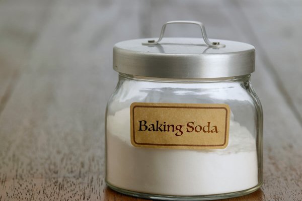 A jar of baking soda on a wooden surface.