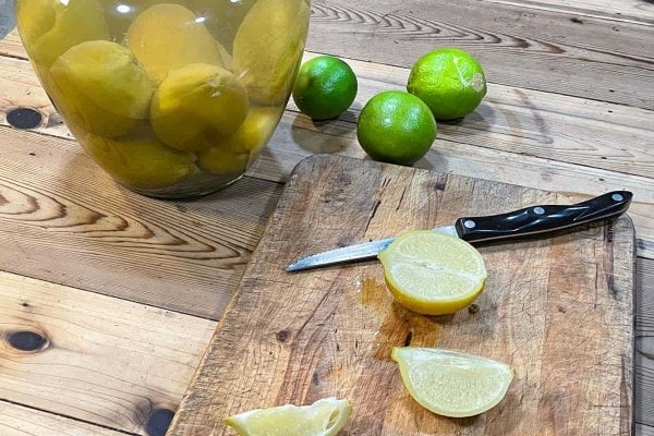 Sliced fermented limes on a cutting board with crock in background.