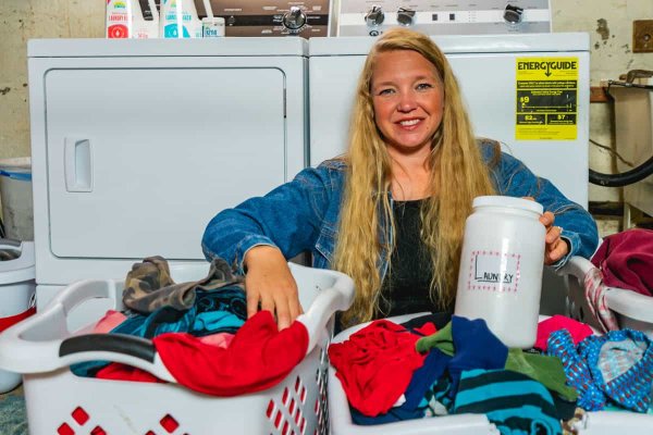 A woman buried in laundry sitting in front of a washer and dryer.