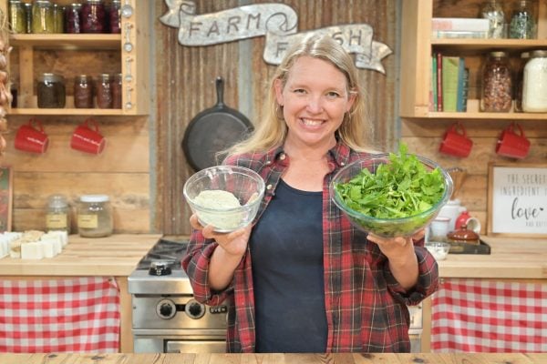 A woman holding a bowl of celery salt and a bowl of celery leaves.