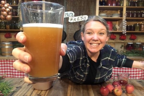 A woman holding up a glass of sparkling apple cider up to the camera.