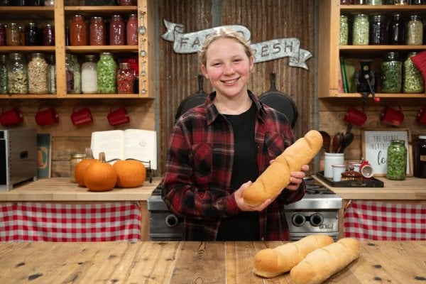 A young girl holding up a loaf of French bread.