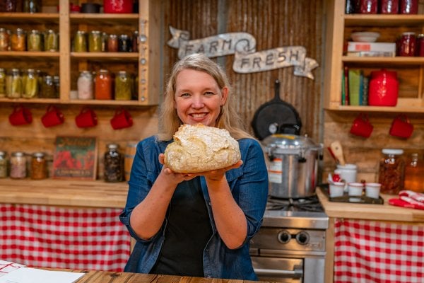 A woman holding up a loaf of fresh baked artisan bread.