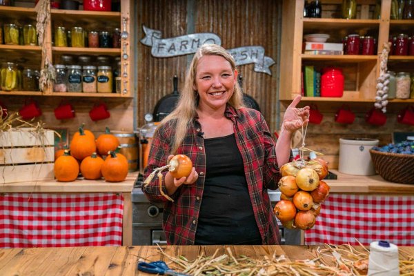A woman holding up an onion in one hand and a bunch of onions strung together in the other.