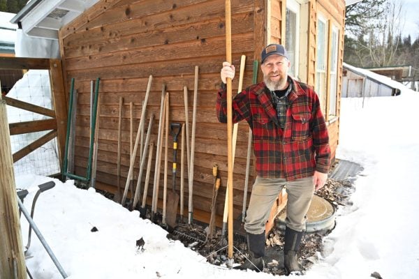 A man standing outside next to a number of garden tools.