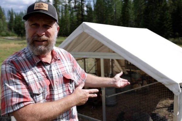 A man pointing to a mobile chicken coop.