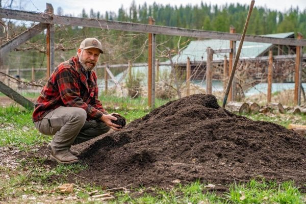 A man by a compost pile with a handful of finished compost.