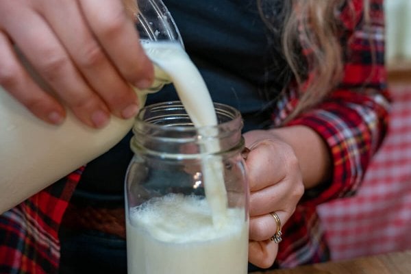 A woman pouring a glass of raw milk into a Mason jar.