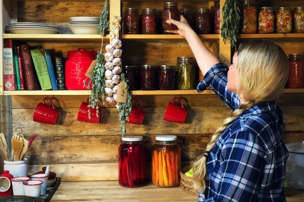 Woman reaching for a jar of food from a shelf up high.