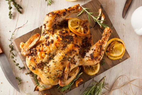 A roasted chicken with lemon slices on a cutting board.