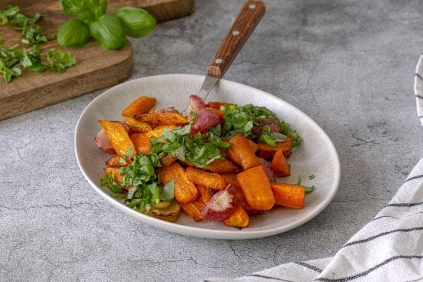 Roasted radishes and carrots on a plate garnished with fresh herbs.