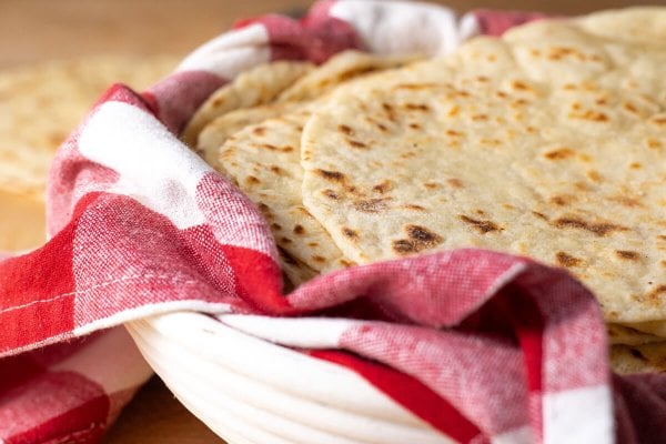 Sourdough discard tortillas stacked in a basked lined with a red and white checkered tea towel.