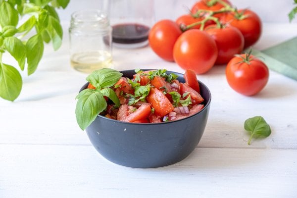 Tomato and onion salad served in a black bowl and garnished with fresh basil leaves.