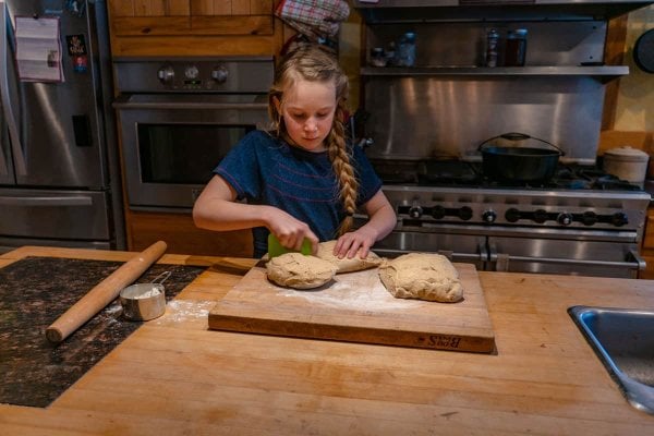 Young girl cutting bread dough on a cutting board.