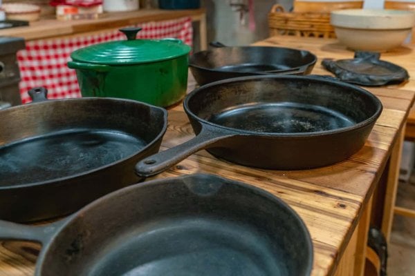Side view of cast iron pots and pans sitting on a wooden table.