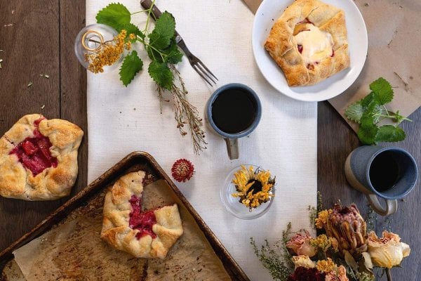 Overhead view of plum pies, coffee mugs, greenery and autumn flowers.